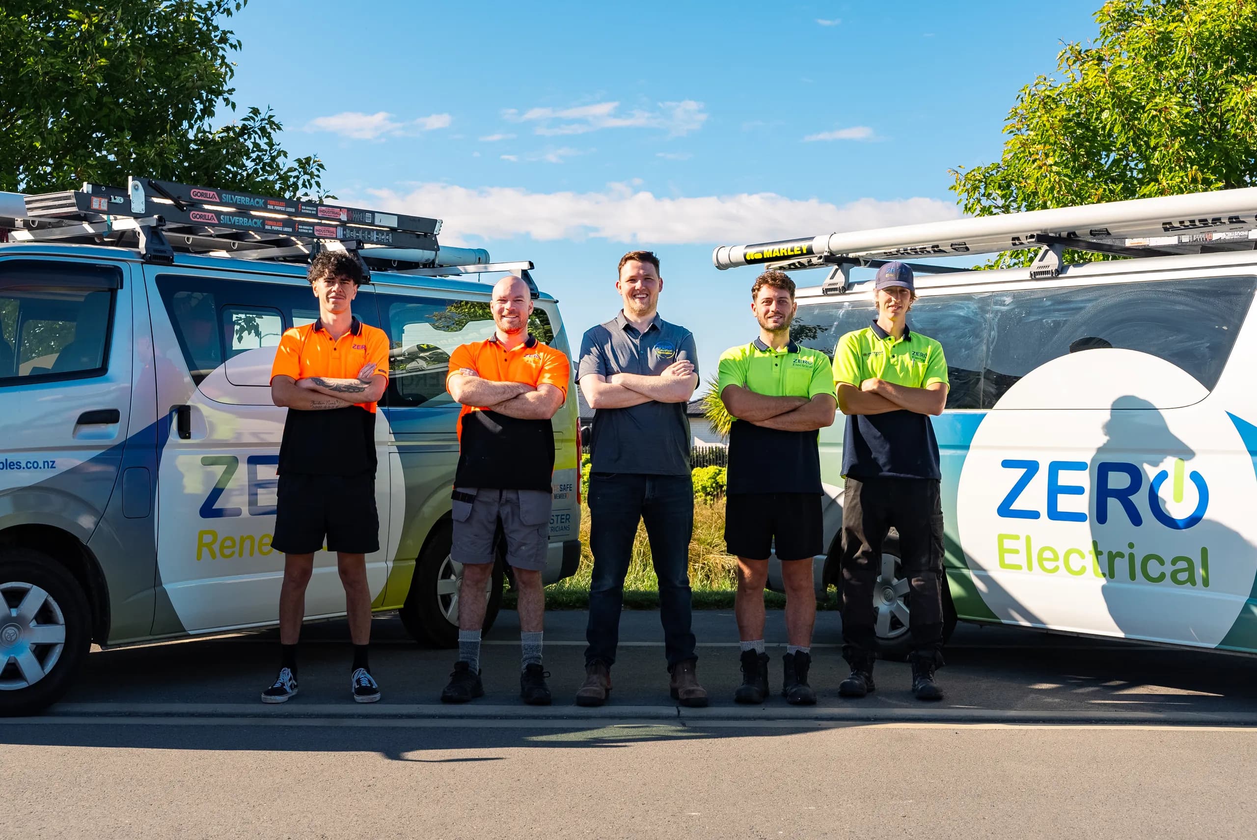 Five smiling ZERO team members in hi-vis stand arms-folded shoulder to shoulder in front of the branded company vans.