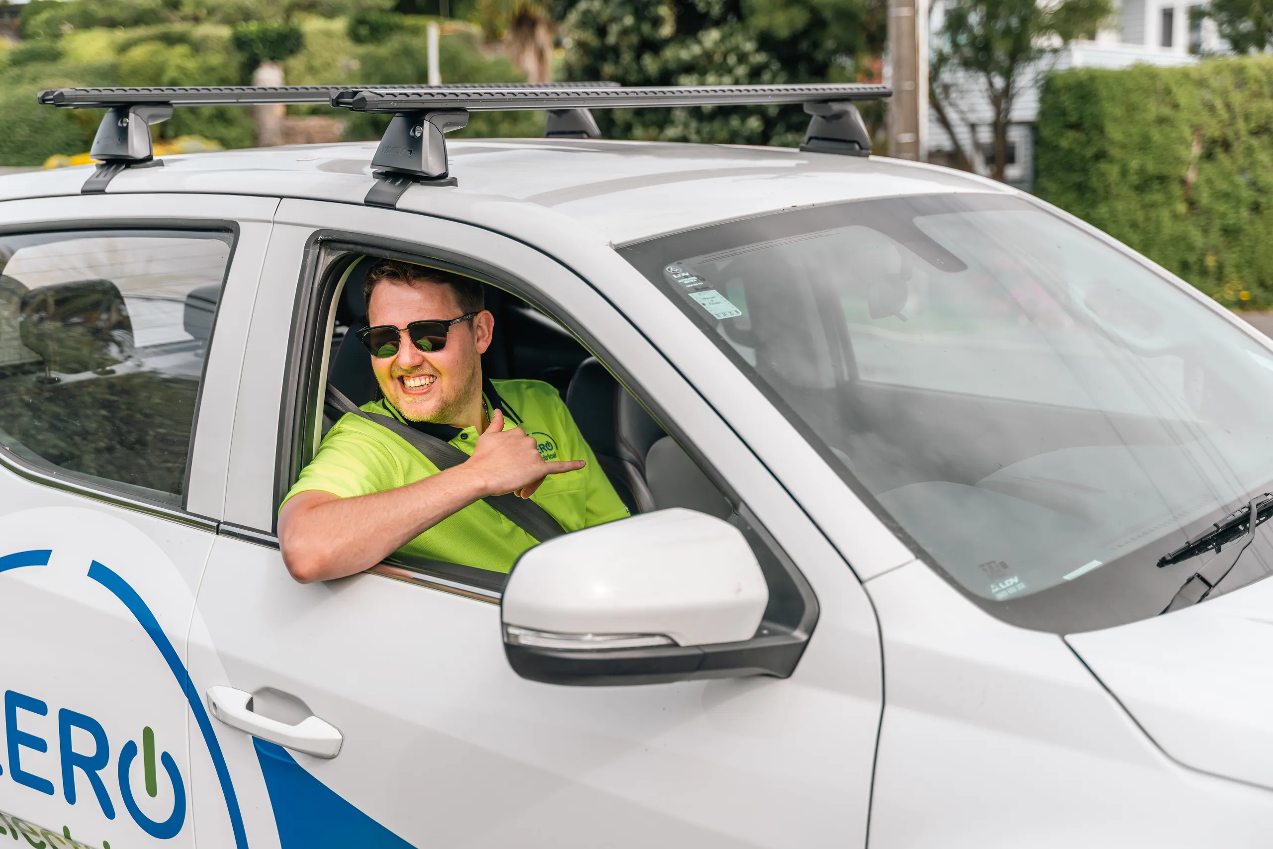 A ZERO team member in sunglasses smiles and gives a shaka from the driver's seat of the branded company ute.