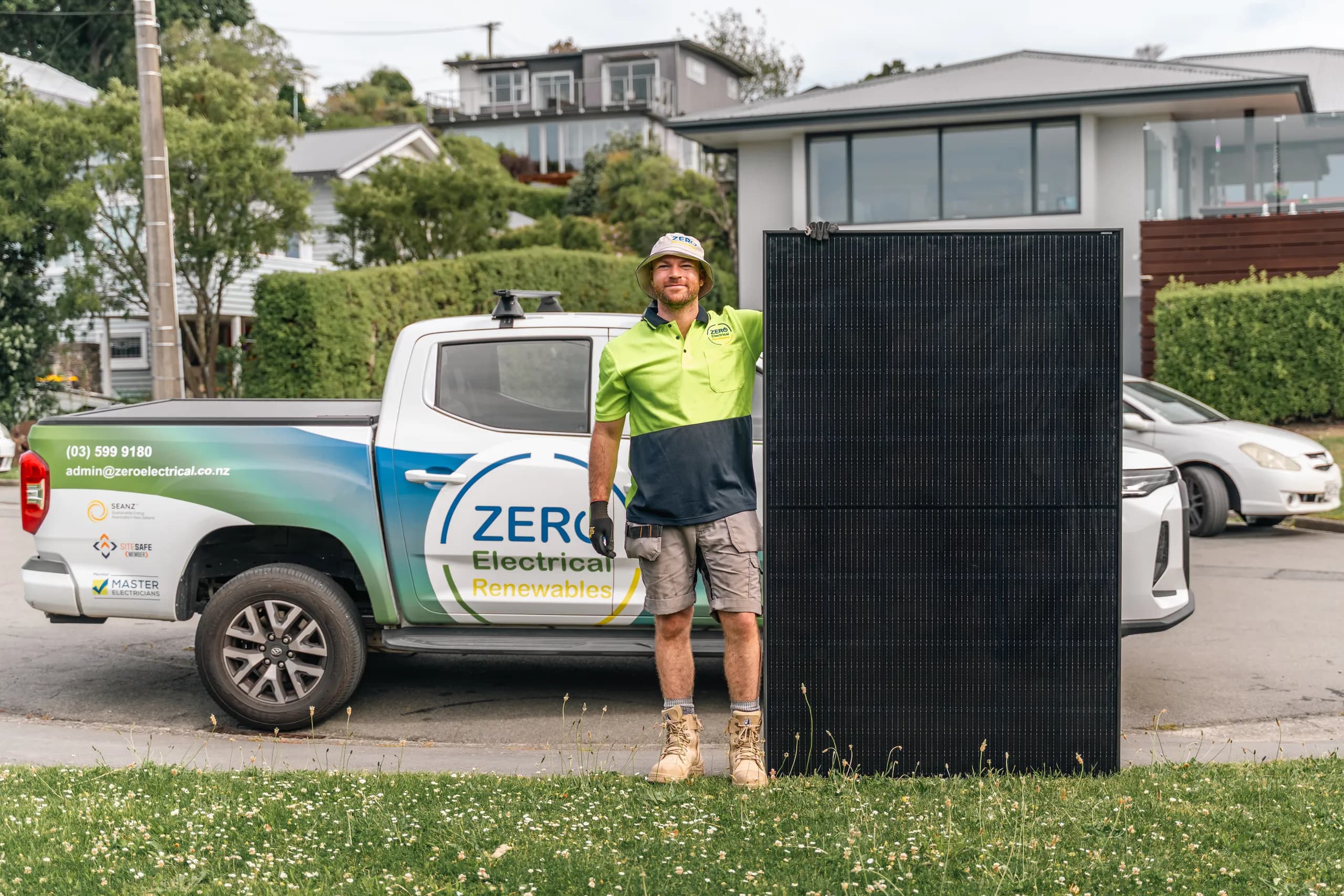 A ZERO team member in a branded bucket hat stands with a solar panel beside the fully branded ZERO Electrical Renewables ute.